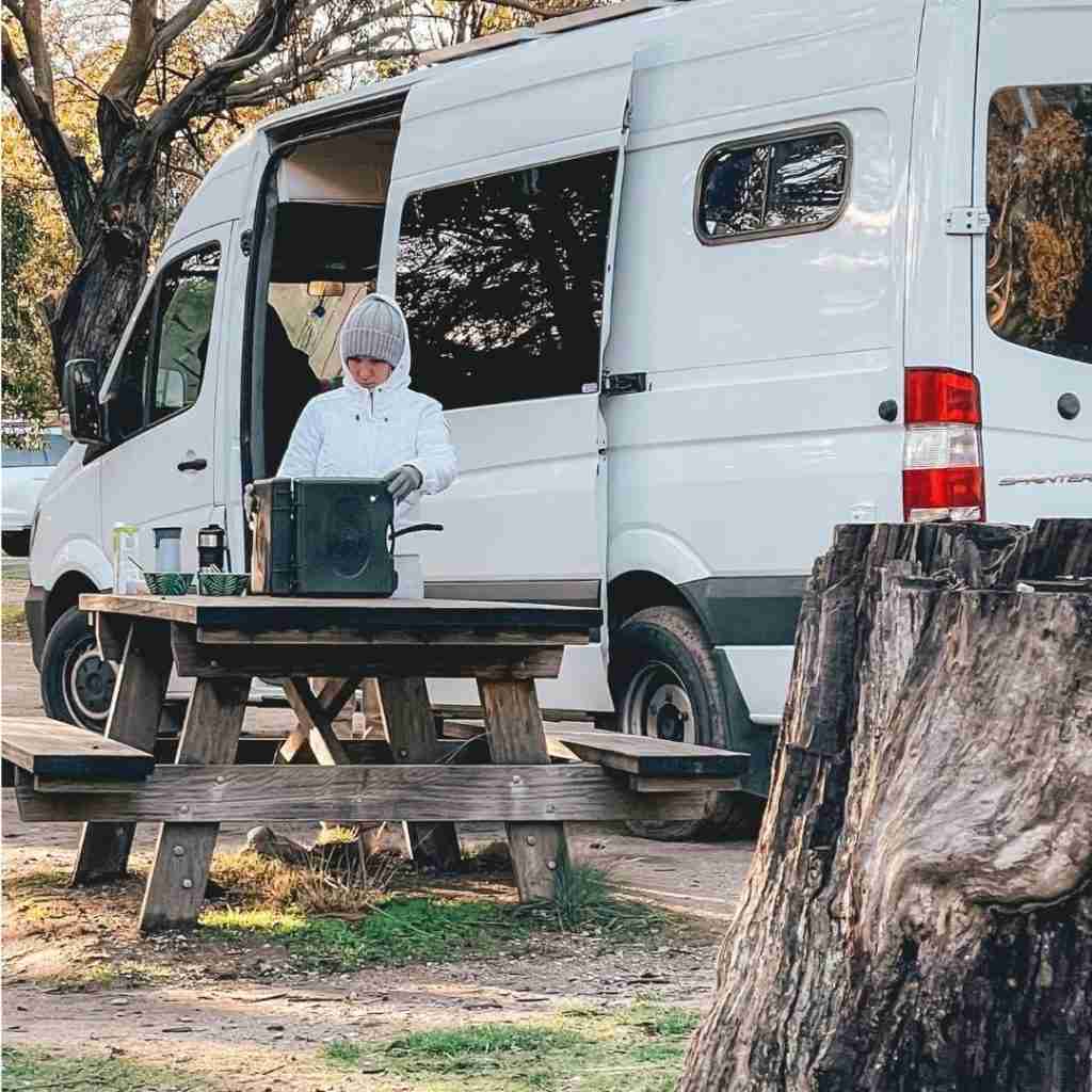 A lady free camping and cooking outside a campervan