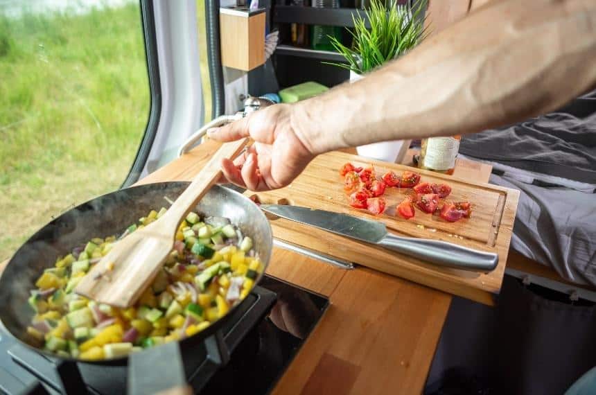 man cooking food inside a campervan 