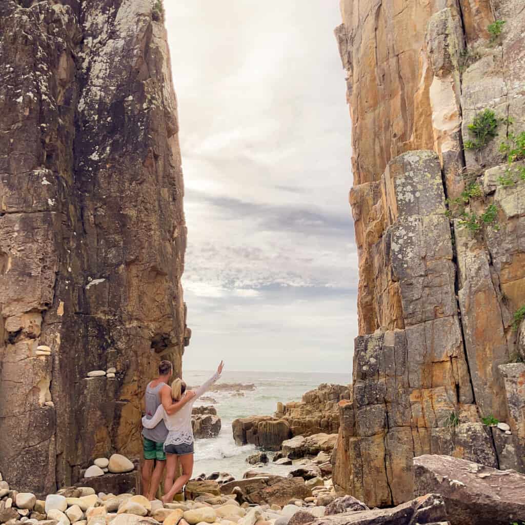 2 people looking out into the ocean with rocks around 