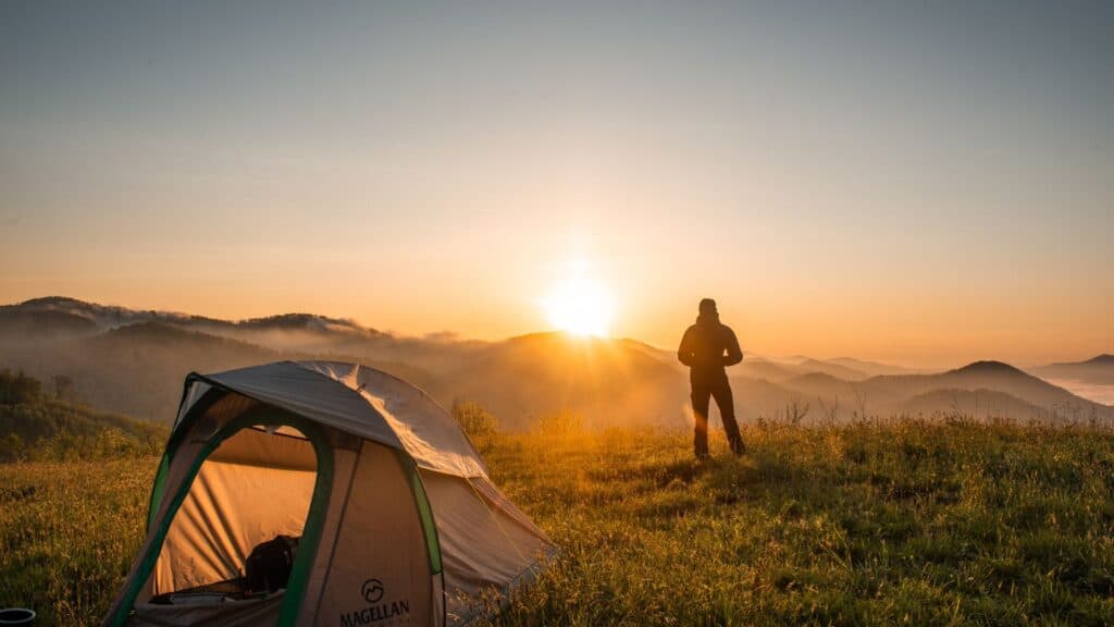 Man watching the sunrise with a tent behind him
