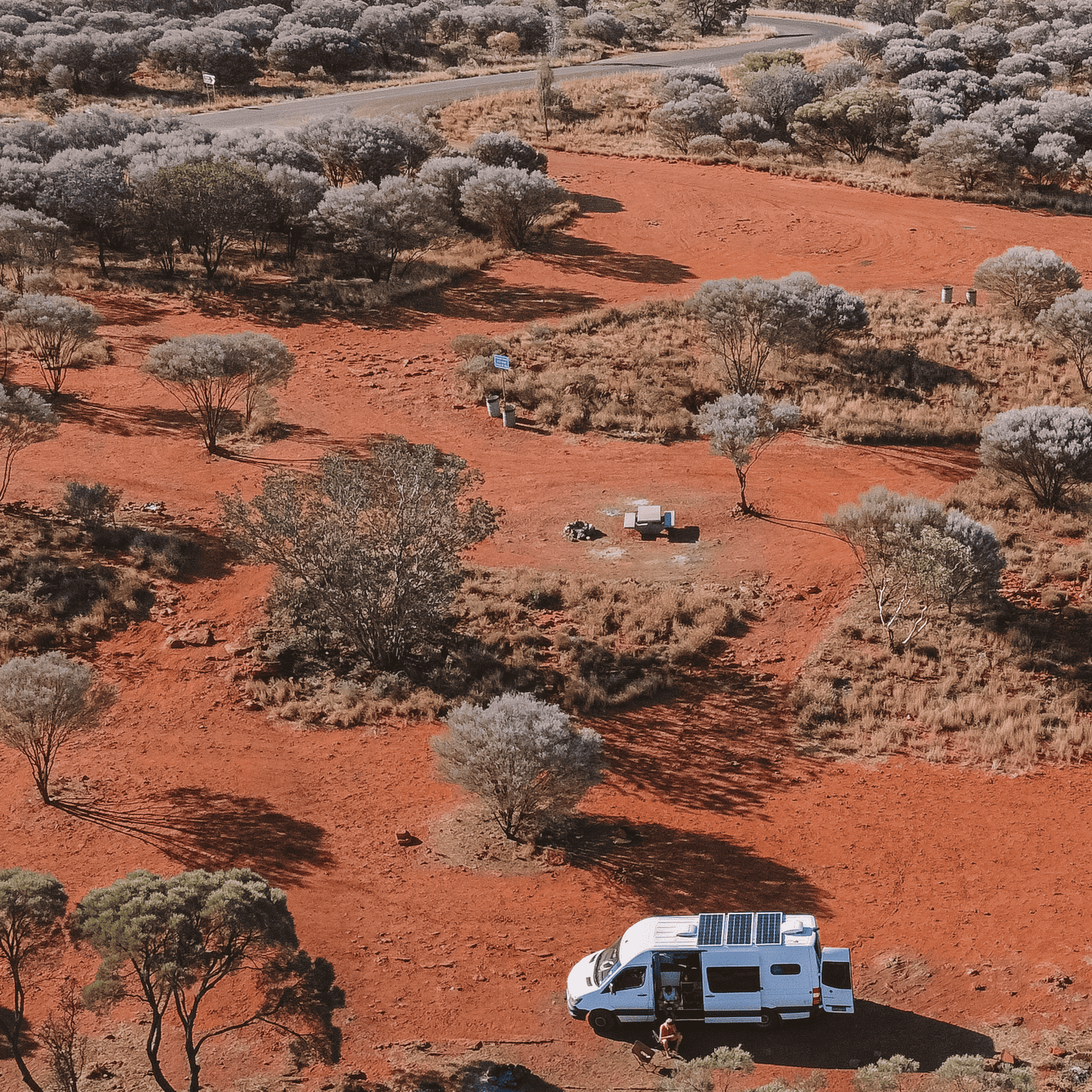 Our campervan parked at a campground that is made of red dirt and looks like the desert. 