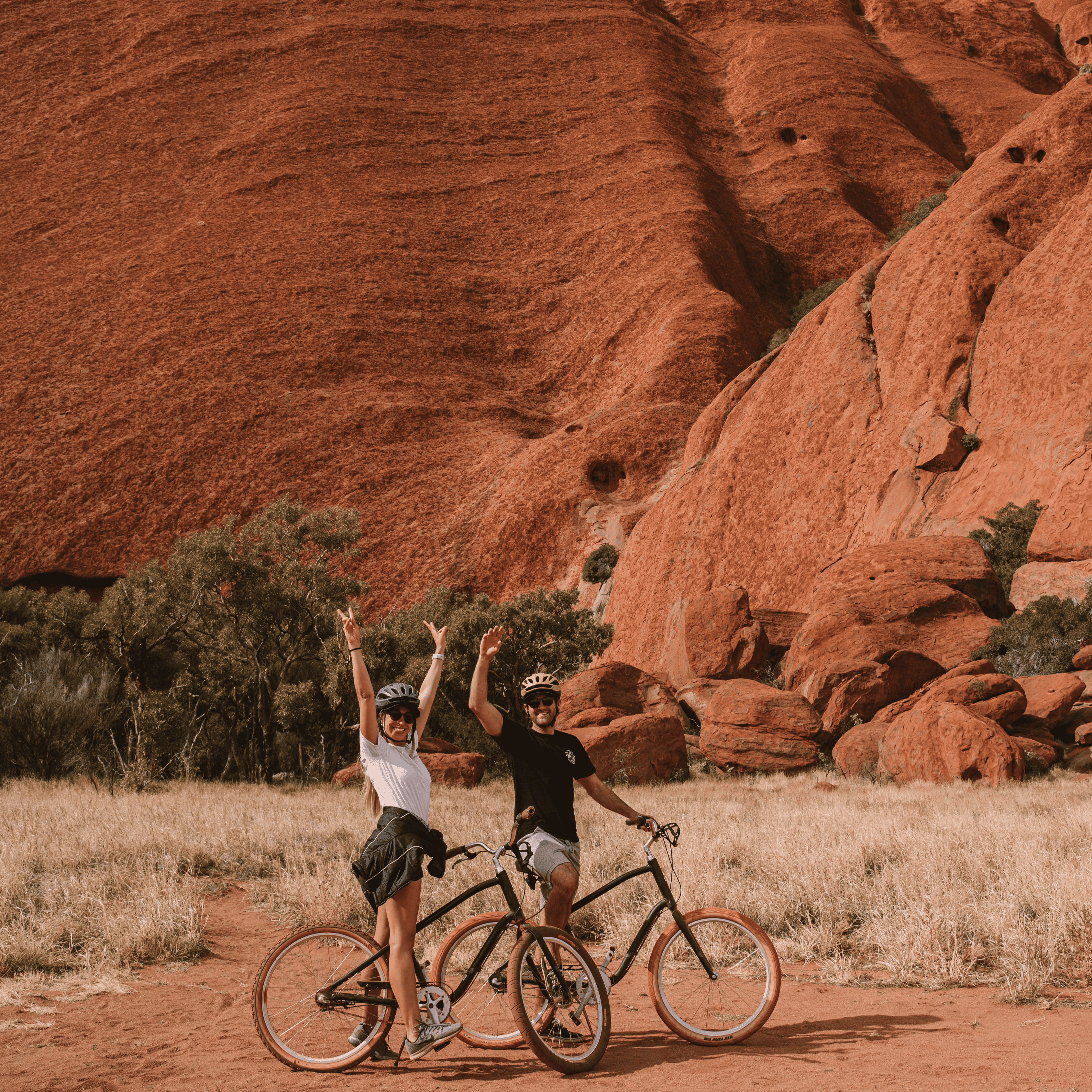 Wade and Dani with their hands up and on top of a bike in front of Uluru