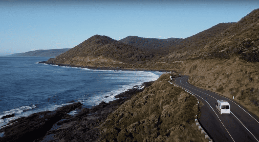 A campervan driving along the Great Ocean Road with the ocean to its left