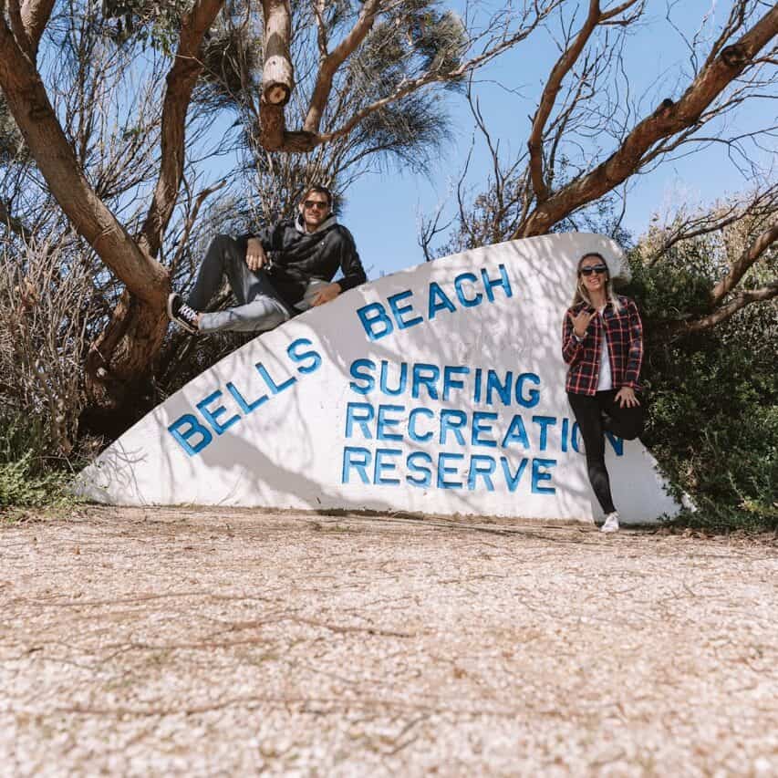Wade and Dani by the Bells Beach entrance sign that reads: "Bells Beach Surfing Recreation Reserve" 