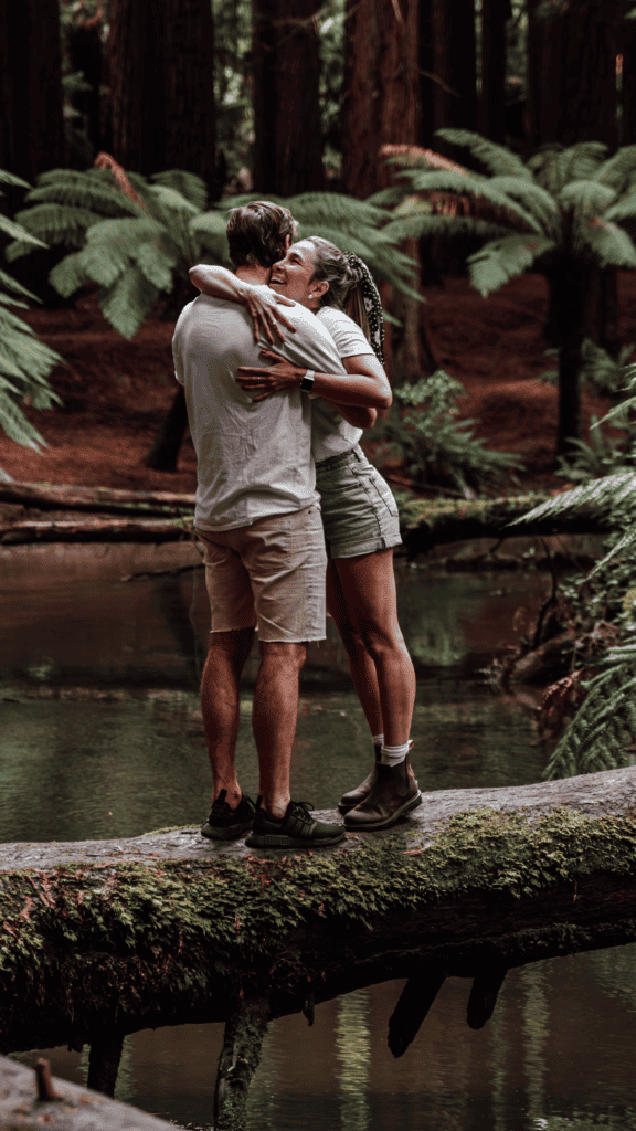 Wade and Dani hug on top of a tree log that is fallen across the river