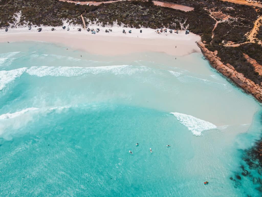 Cars parked in line at Wharton Beach where the sand is very white and water turquoise blue