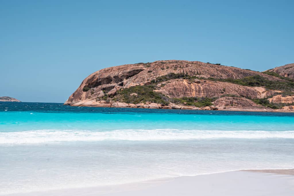 A picture of the right end of the beach in Lucky Bay. There is a rocky mountain at the end of the beach, with white sand and crystal clear water. 