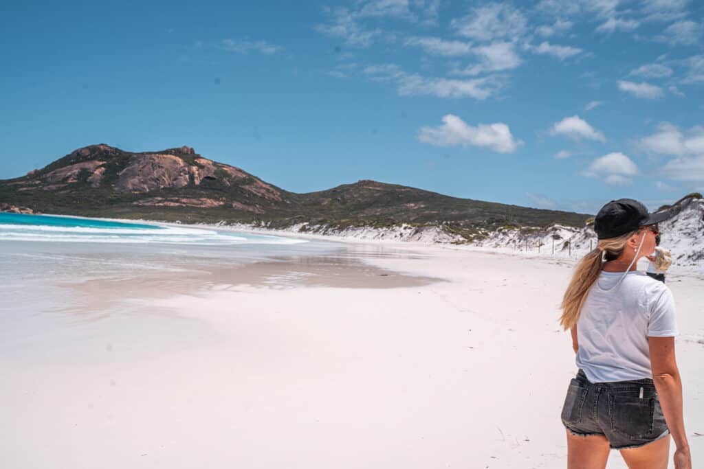 Dani walking on the beach in Hellfire Bay. The sand is very white and the water very blue. You can see a mountain in front of us