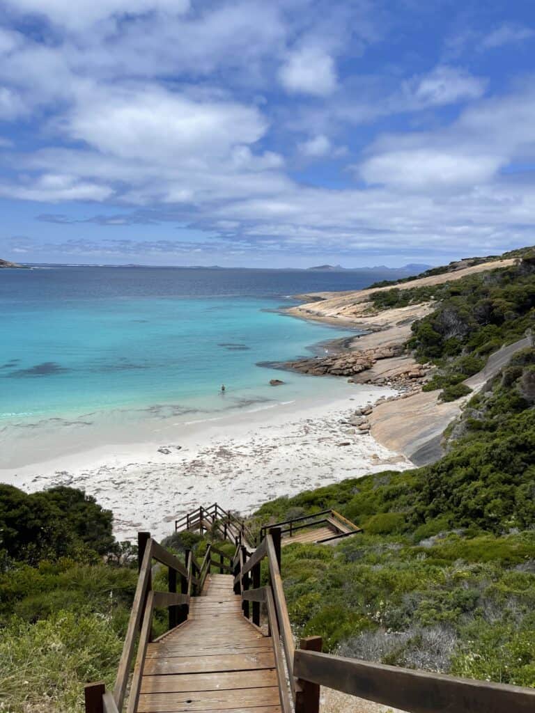 Wooden Steps taking you down to BLue Haven Beach where the sand is white, turquoise water and rocks on the right hand side.