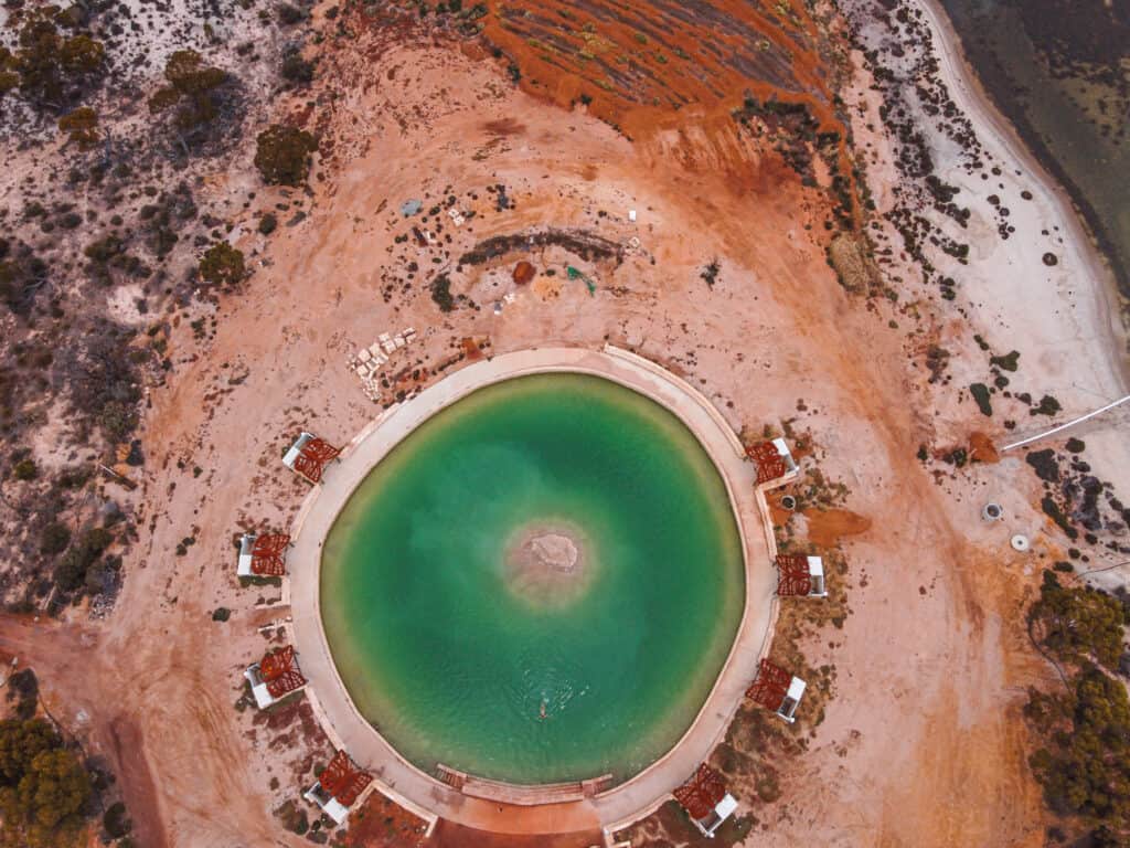 A drone picture of Lake Magic. The water is green and the lake is round with huts all around it