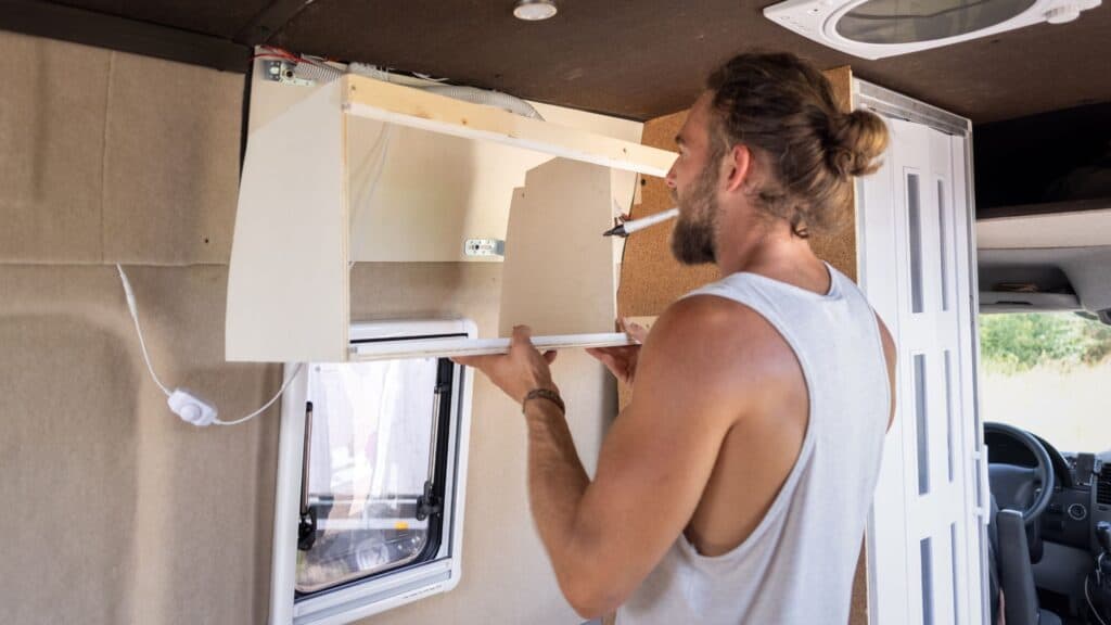 a Man installing a wall cabinet inside a caravan 