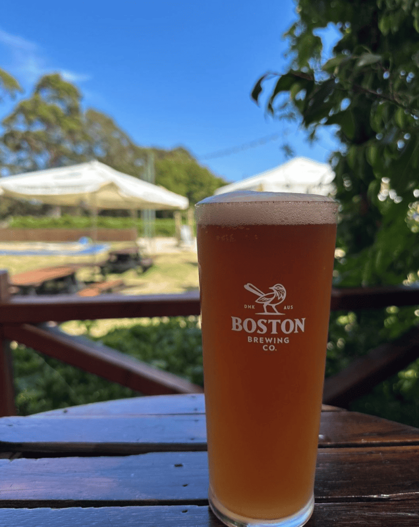 A beer on a table with the brewery as the view