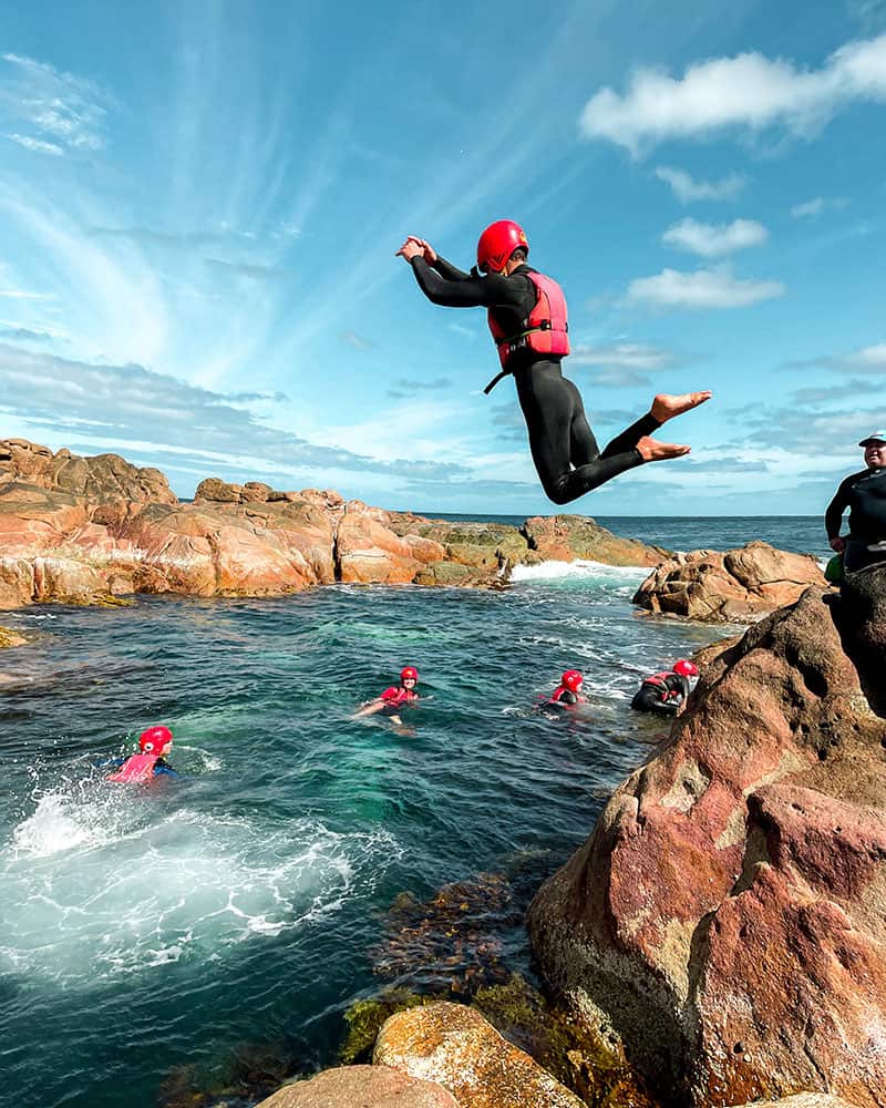 Image of a group of people practicing Coasteering. One person is jumping in the water from the rocks
